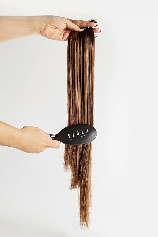 Brown hair extensions being held with a black comb labeled 'Viola' on a white background